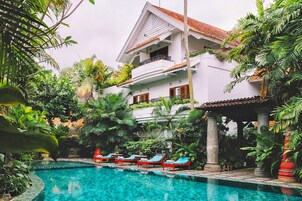 Un edificio de dos plantas con piscina rodeada de abundante vegetación.