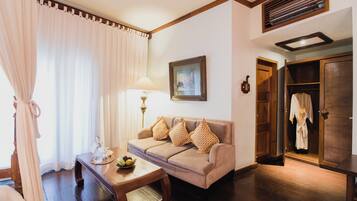 A living room with a sofa, a table with a bowl of fruit, a lamp, and a wardrobe.