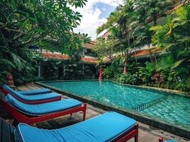 Un área de piscina con sillones de descanso y exuberante vegetación tropical.