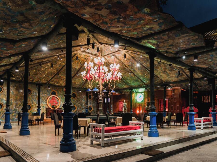 A spacious hall with a high ceiling, ornate chandeliers, and a central seating area with a red bench.