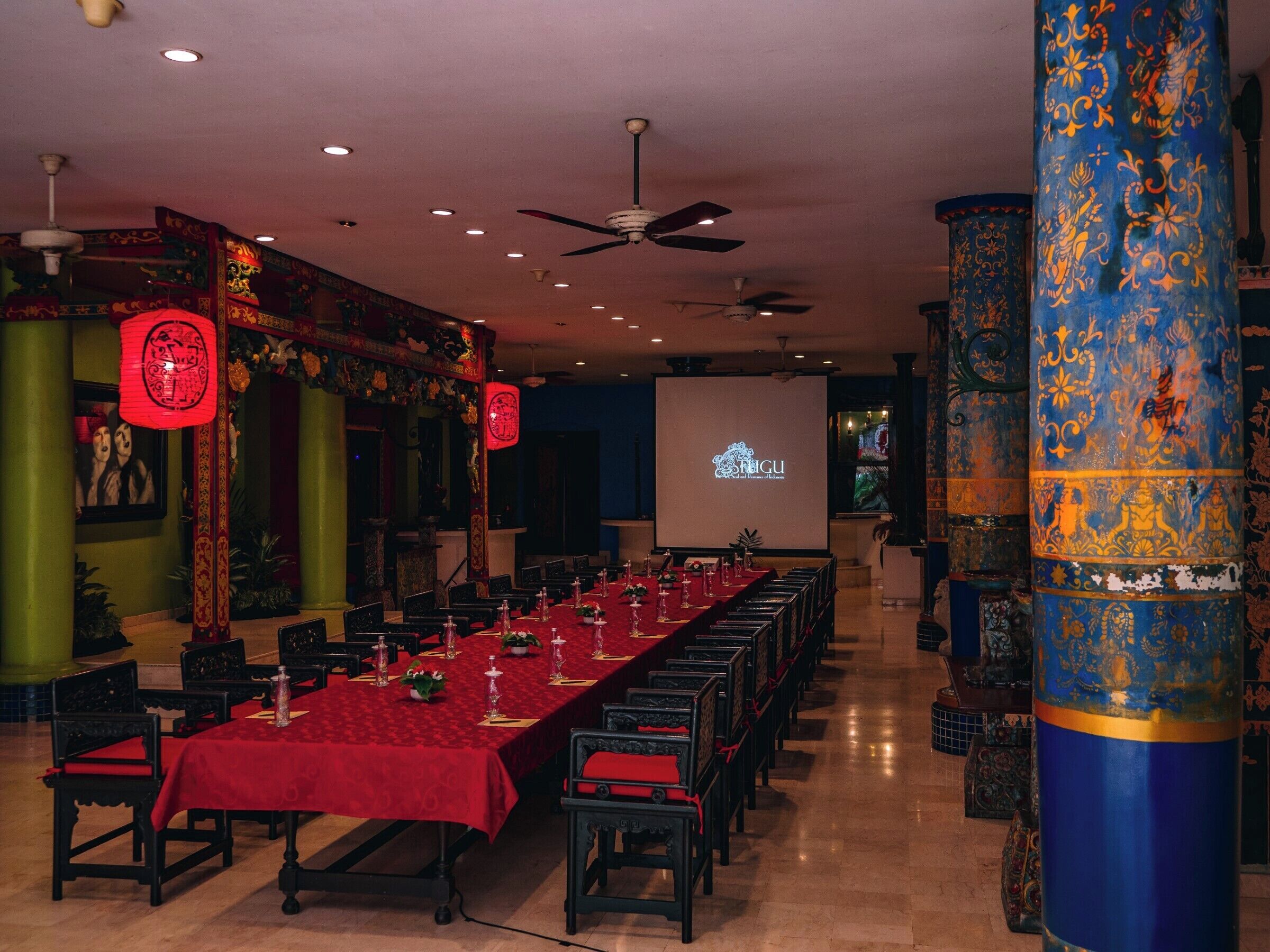 A banquet hall with a long table set for a formal event, adorned with red tablecloths and traditional decor.