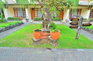 A garden with a statue, a signpost with directions, and a building in the background.