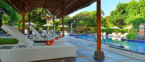 A poolside area with lounge chairs, a covered seating area, and a pool.