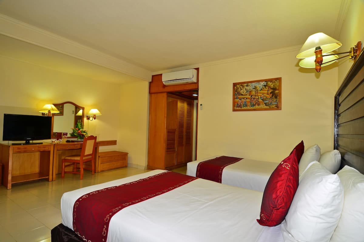A hotel room with two beds, a desk with a chair, a television, and an air conditioning unit.