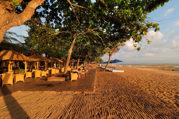 A beachside restaurant with outdoor seating, palm trees, and a wooden deck. - Inna Sindhu Beach (Denpasar)