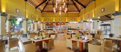 A spacious dining area with high ceilings and a central chandelier, featuring multiple tables and chairs.