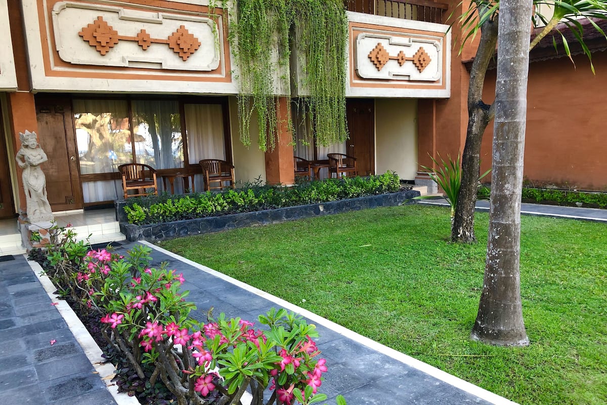 A courtyard with a well-maintained lawn, a flower bed with pink flowers, and a seating area with wooden furniture.