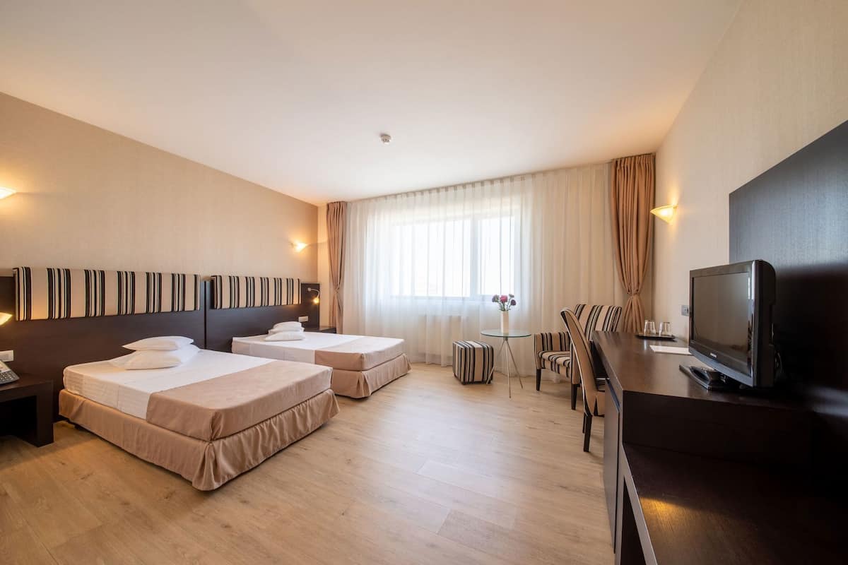 A hotel room with two beds, a TV, a desk, and a dining area.