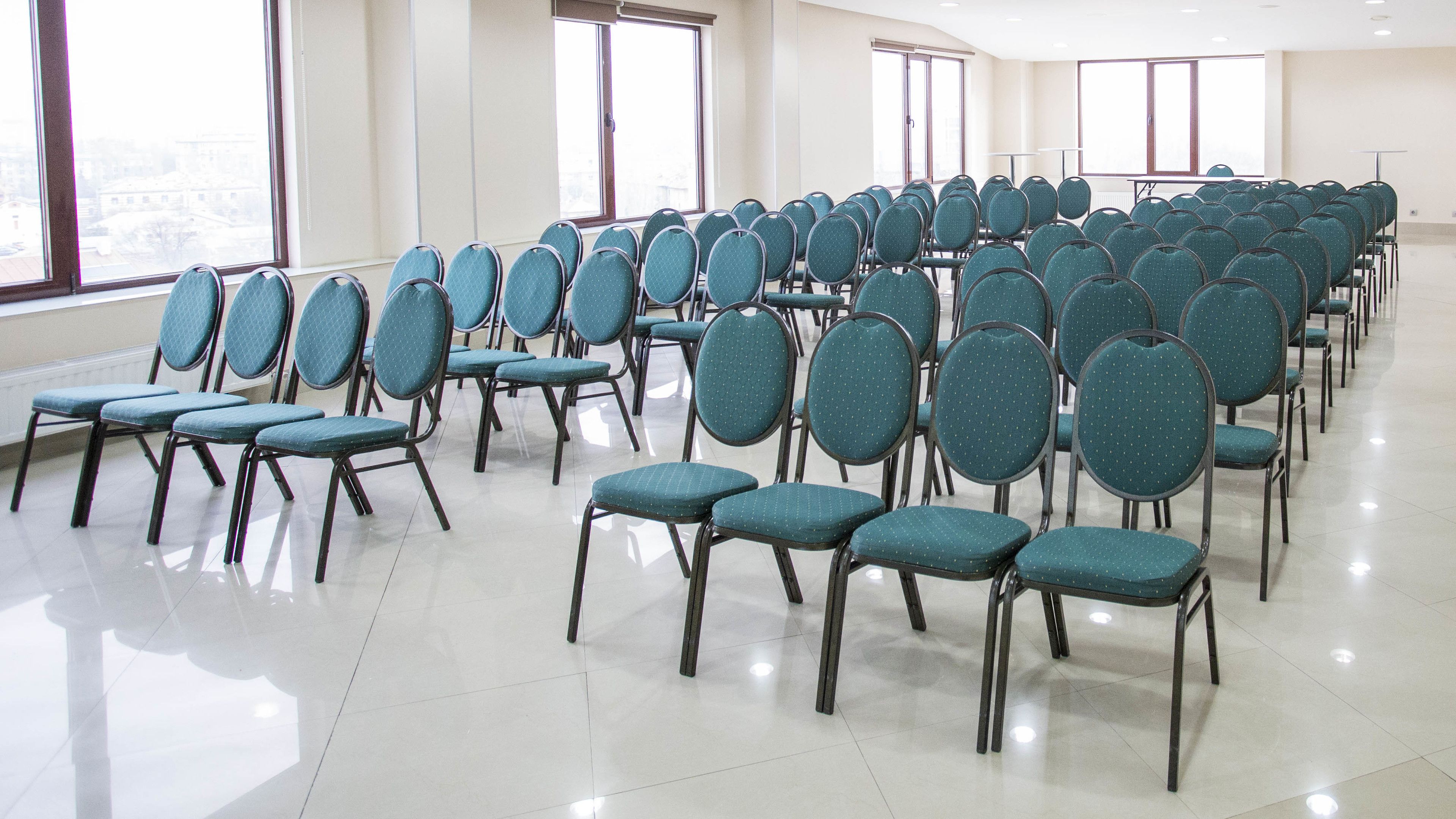 Un salón de conferencias con hileras de sillas color turquesa y un amplio ventanal que proporciona luz natural.