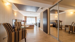 Una habitación de hotel moderna con un espejo grande, sillones a rayas, una mesa de comedor y un sofá.