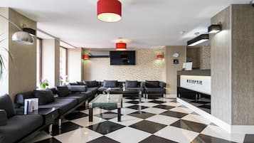 Een moderne lobby met een zwart-wit geruite vloer, zwarte banken, een receptiebalie en een grote rode hanglamp.