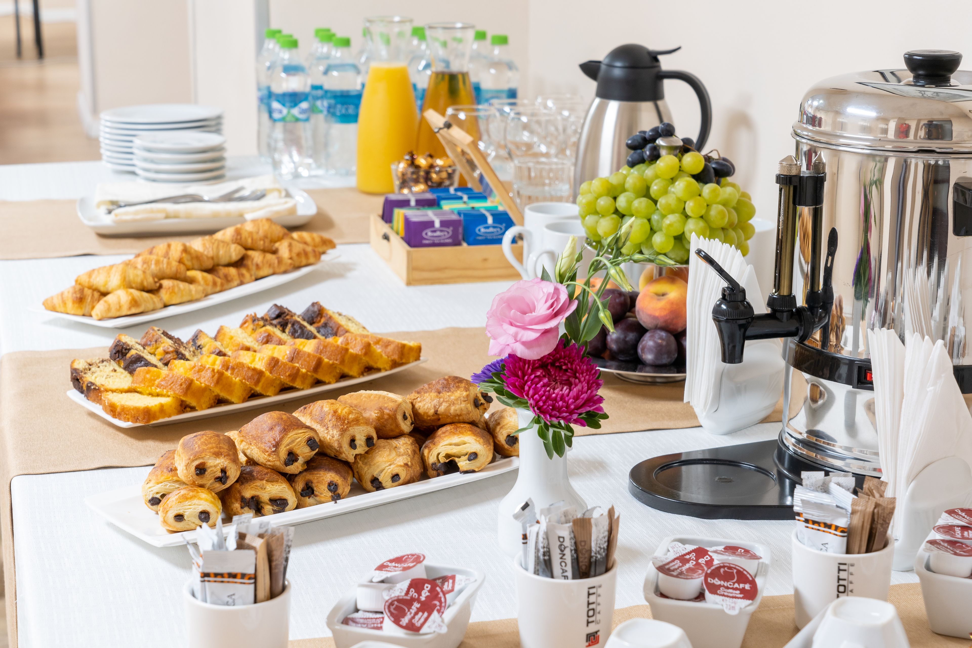 A breakfast buffet with pastries, fruits, and beverages.