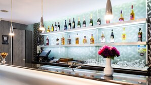 Una zona de bar con estantes llenos de botellas de licor, una caja registradora y un jarrón con flores.