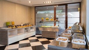 Un área de bufé con diversos alimentos y bebidas, suelo a cuadros y una vitrina de cristal.