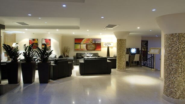 A modern lobby with a seating area, potted plants, artwork, and a television. - The Windsor Hotel (Sliema)