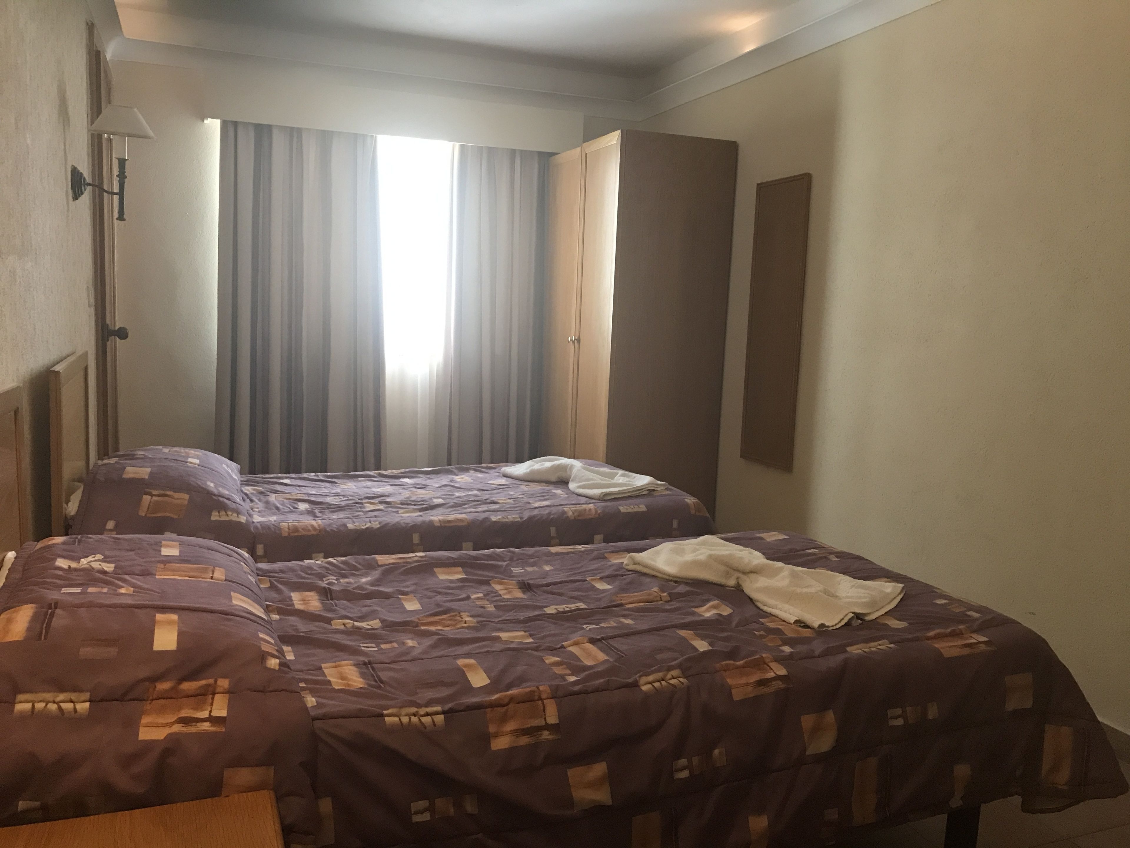 Una camera d'albergo con due letti, un comodino, una lampada e una finestra con tende.