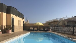 A swimming pool with lounge chairs and a yellow umbrella, surrounded by buildings and a metal fence. - The Windsor Hotel (Sliema)