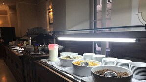 A buffet setup with various food items and bowls on a counter, illuminated by a bright overhead light. - The Windsor Hotel (Sliema)