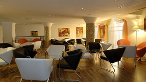 A modern interior with multiple seating areas, including white and black chairs, and a wooden floor. - The Windsor Hotel (Sliema)