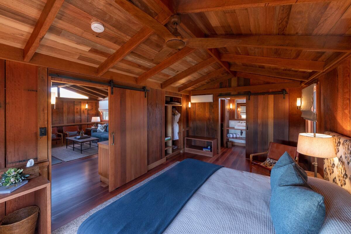 A spacious room with a large bed, a wooden ceiling, and a view of a dining area.