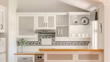 A kitchen with white cabinets, a stove, and a sink. There are decorative plates on the wall and a vase with flowers on the counter.