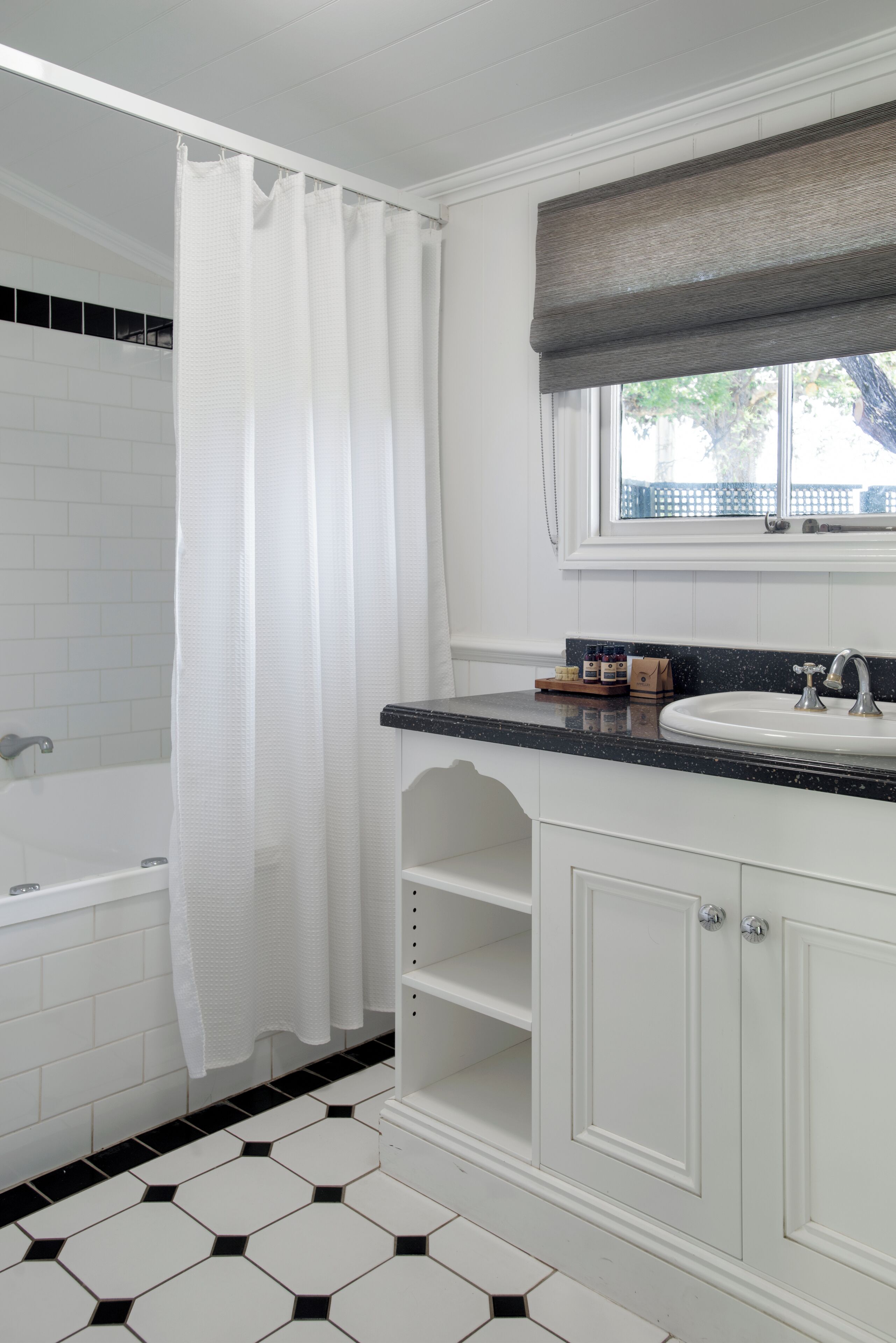 Un baño con una bañera blanca, un lavamanos blanco y una ventana que ofrece vistas a árboles.
