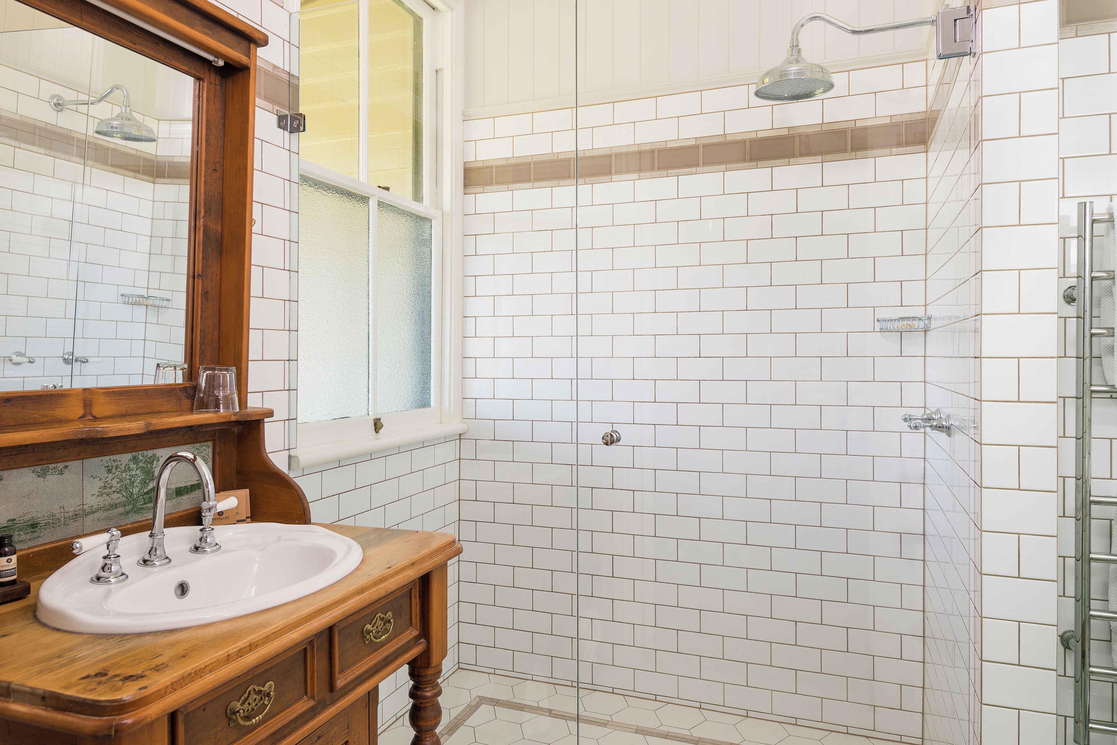 A bathroom with a white-tiled shower, a wooden vanity with a sink, and a large mirror.