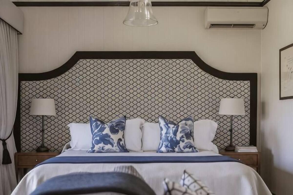 A hotel room with a large bed, two bedside tables, a headboard with a geometric pattern, and a hanging light fixture.