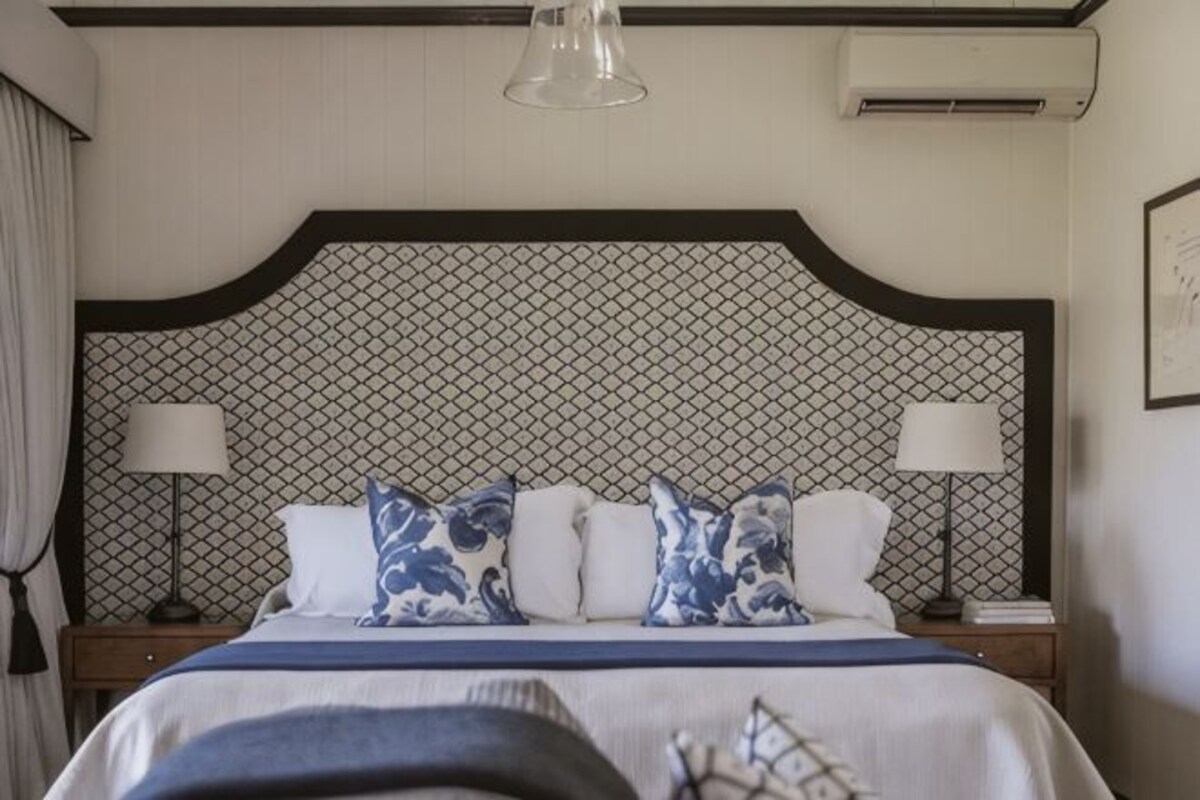A hotel room with a large bed, two bedside tables, a headboard with a geometric pattern, and a hanging light fixture.