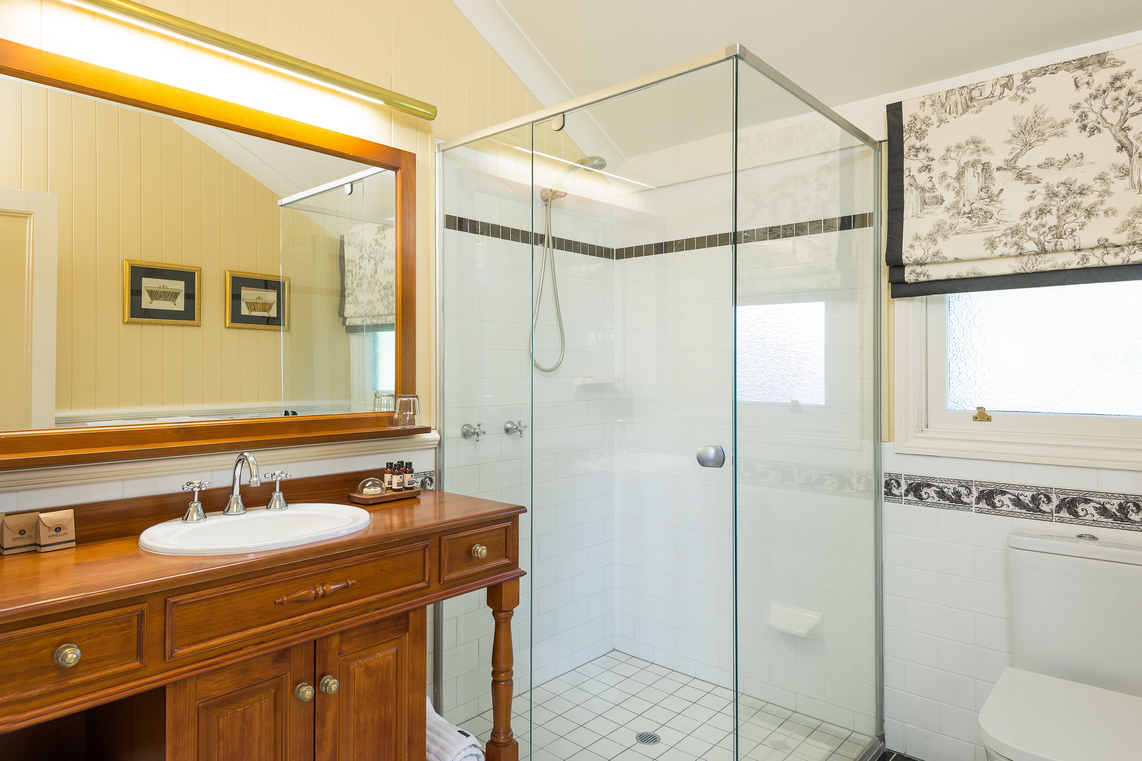 Un baño con tocador de madera, un espejo grande, cabina de ducha de vidrio y un inodoro.