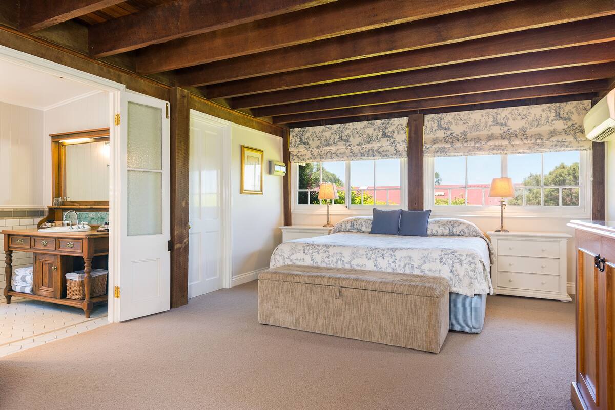A bedroom with a large bed, a nightstand, a dresser, a bench, and a window with a view.