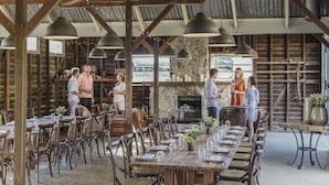 An outdoor dining area with wooden tables and chairs, stone walls, and hanging pendant lights. - Spicers Hidden Vale (Grandchester)