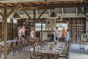 Un área de comedor al aire libre con mesas y sillas de madera, paredes de piedra y lámparas colgantes.