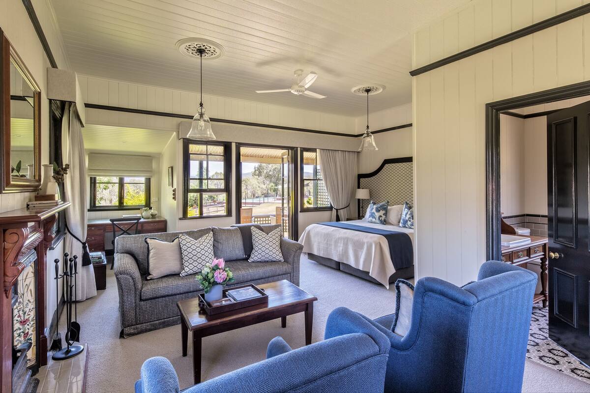 A spacious living area with a sofa, armchairs, a coffee table, and a bed. There are ceiling fans, large windows, and a view of the outdoors.
