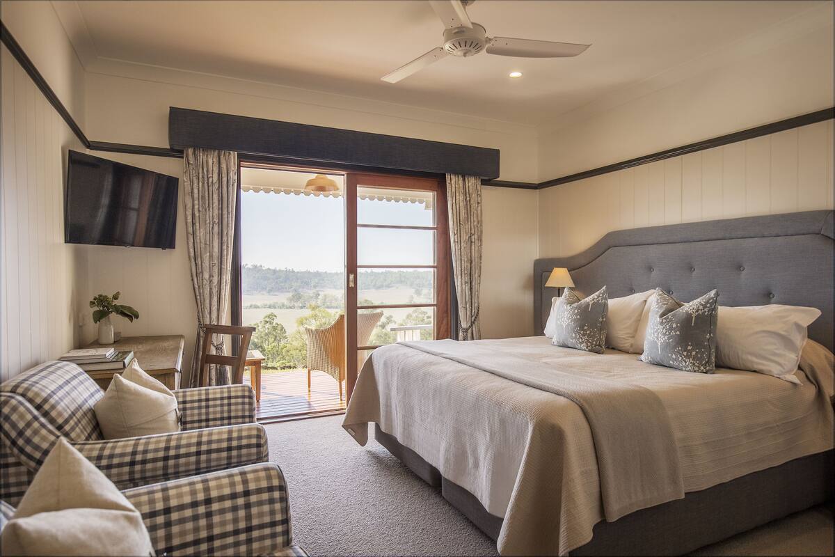 A bedroom with a bed, a ceiling fan, a TV mounted on the wall, and a view of the outdoors through a sliding door.