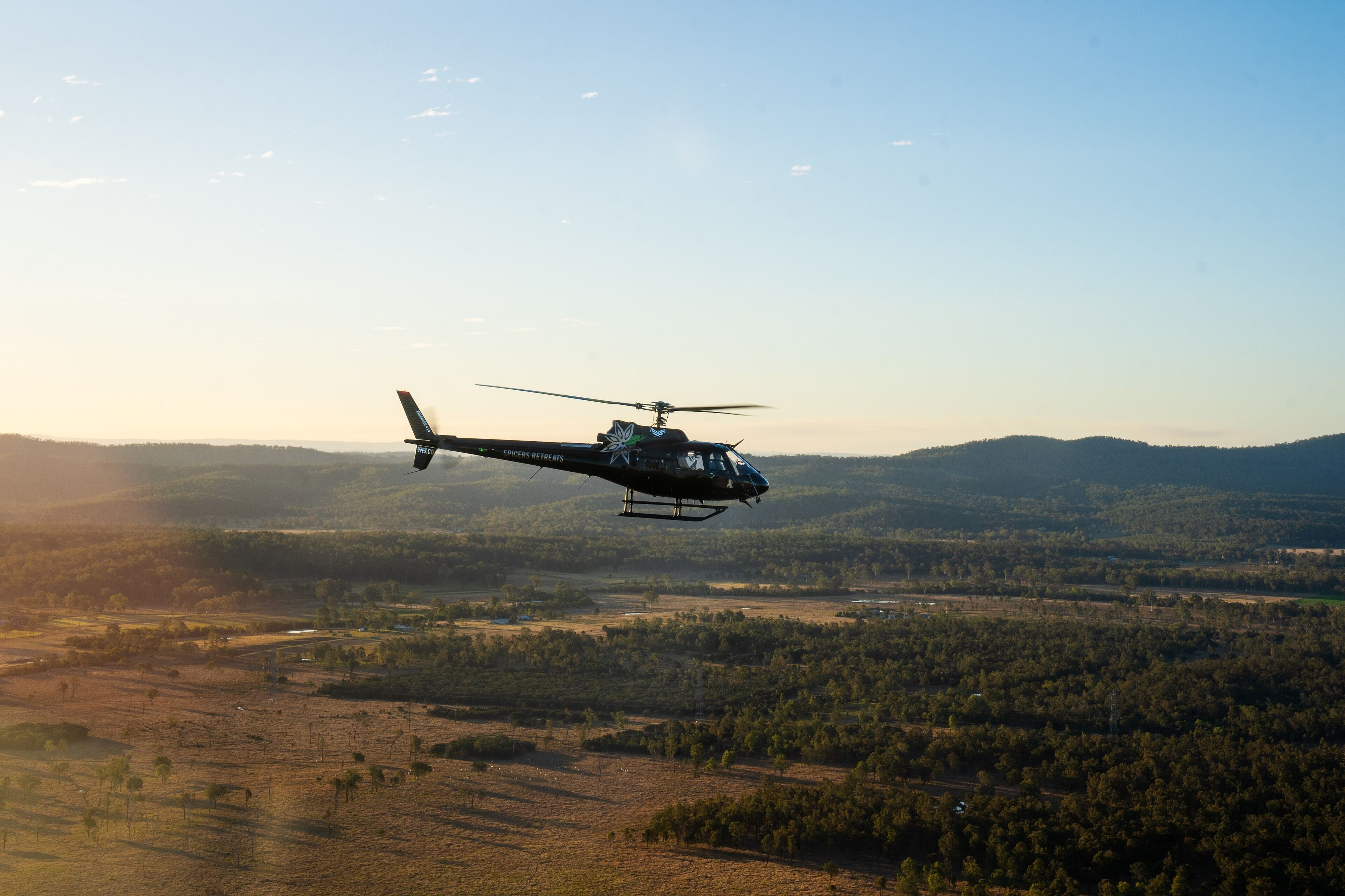 A helicopter flying over a landscape with forests and open fields.