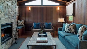 A cozy living room with a stone fireplace, wooden walls, a blue sofa, and a coffee table with books. - Spicers Hidden Vale (Grandchester)