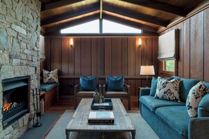 Una sala de estar acogedora con chimenea de piedra, paredes de madera, un sofá azul y una mesa de centro con libros.
