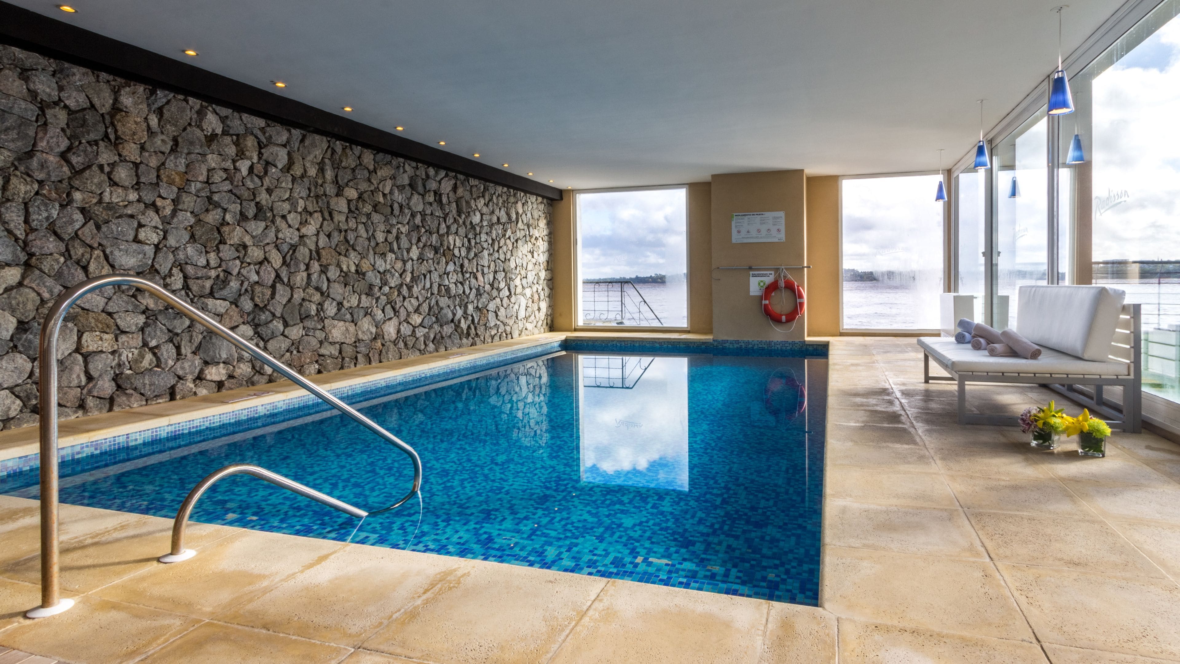 Una piscina amb una paret de pedra, un flotador i una cadira amb tovalloles.