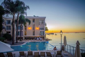 Un hotel con piscina, sillones de descanso y vista al mar al atardecer.