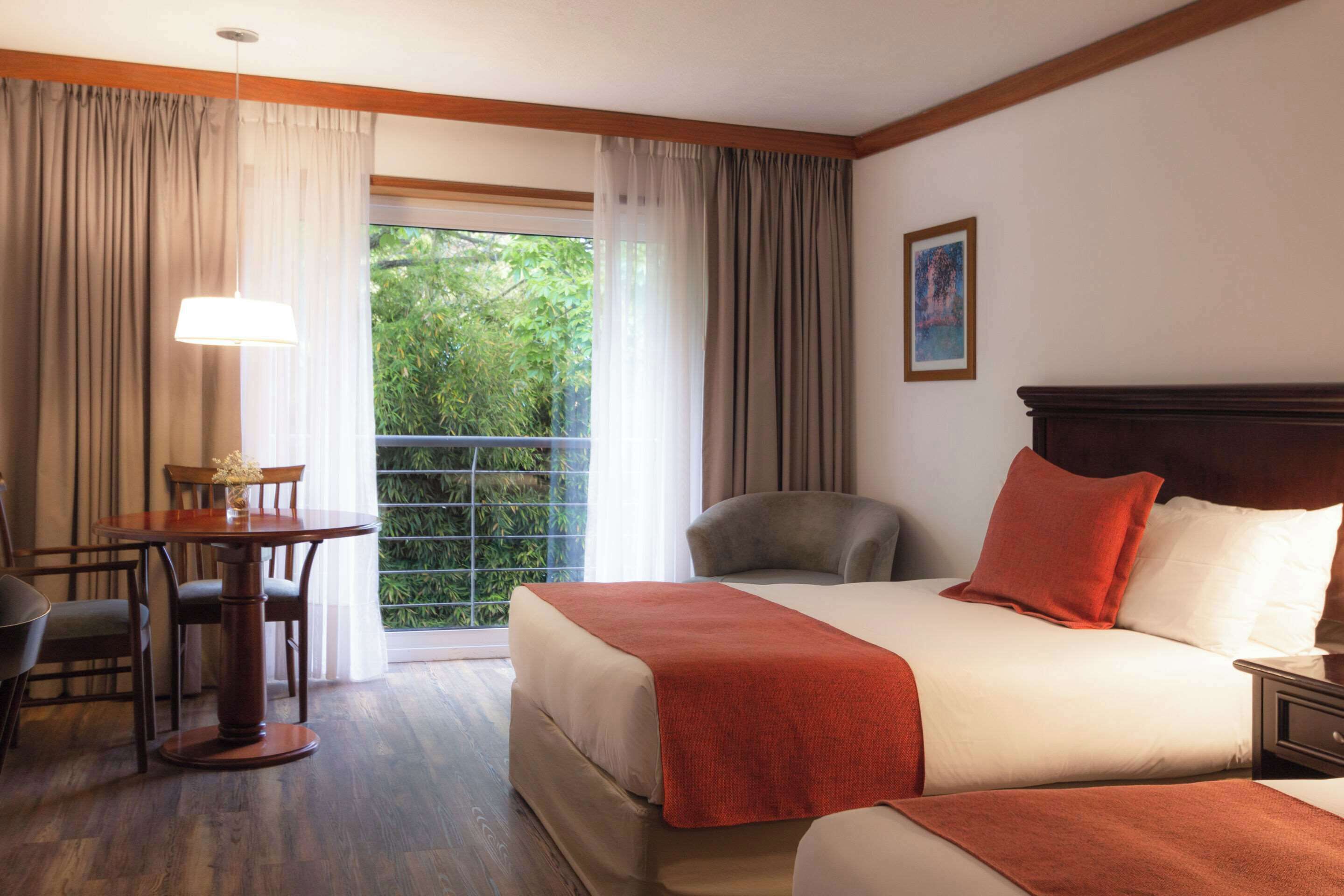 A hotel room with a bed, a desk, a chair, and a window with curtains.