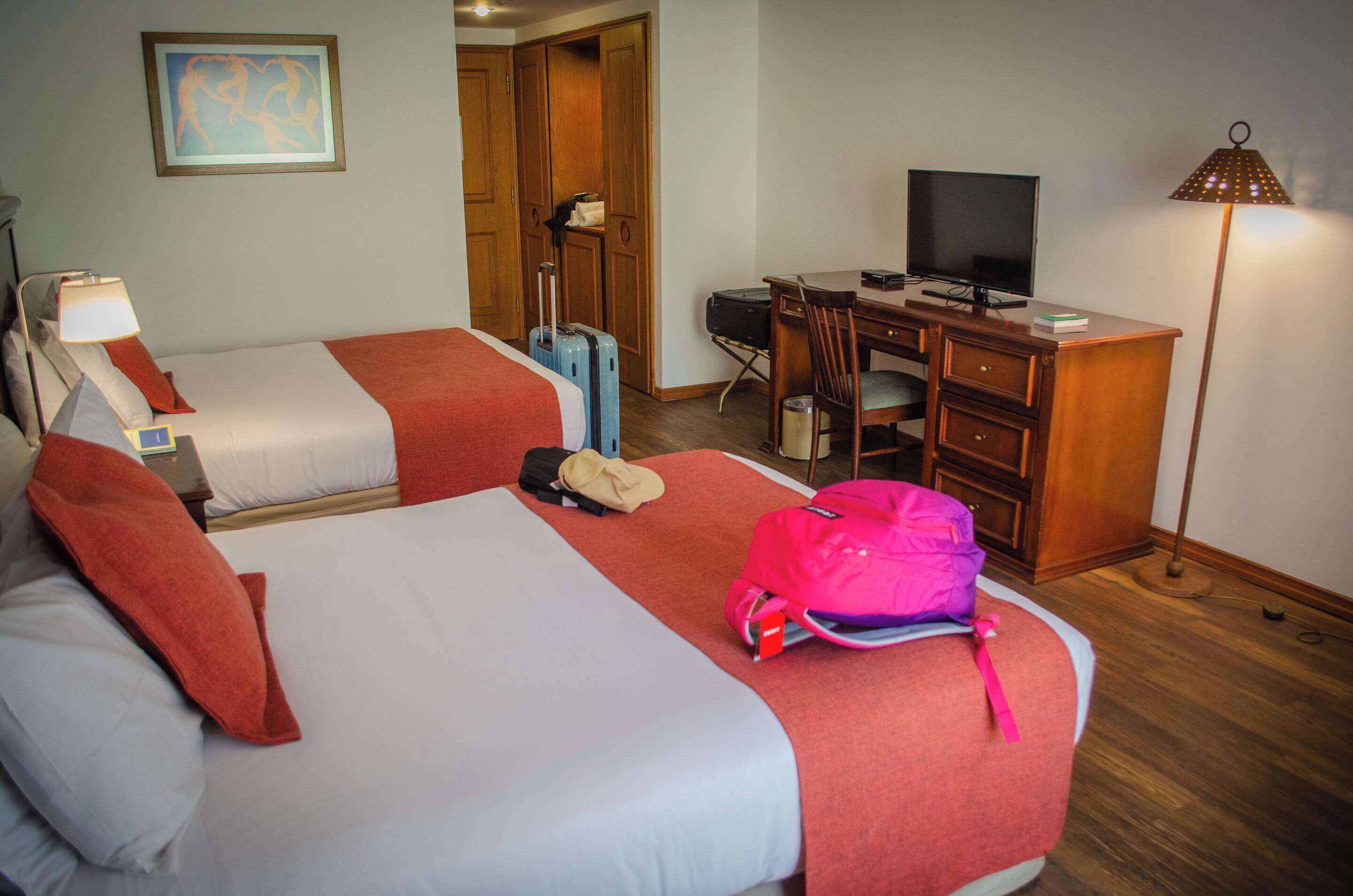 Une chambre d’hôtel avec deux lits, un bureau, une chaise, une télévision et une lampe.