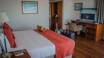 Quarto de hotel com cama, escrivaninha, cadeira, televisão e mala.