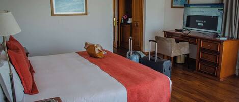 A hotel room with a bed, a desk, a chair, a television, and a suitcase.