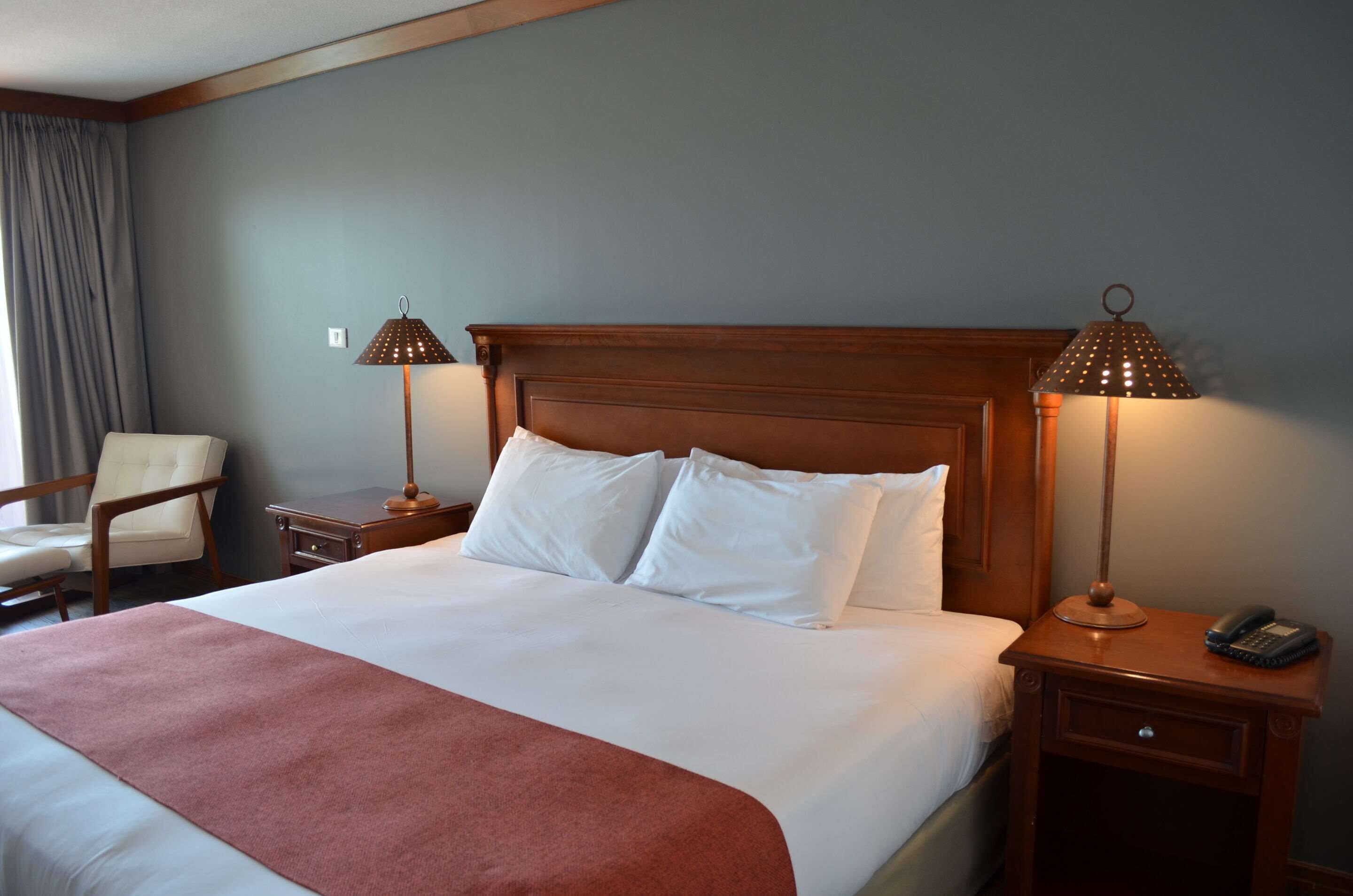Une chambre d’hôtel avec un grand lit, deux tables de chevet, une chaise et deux lampes.