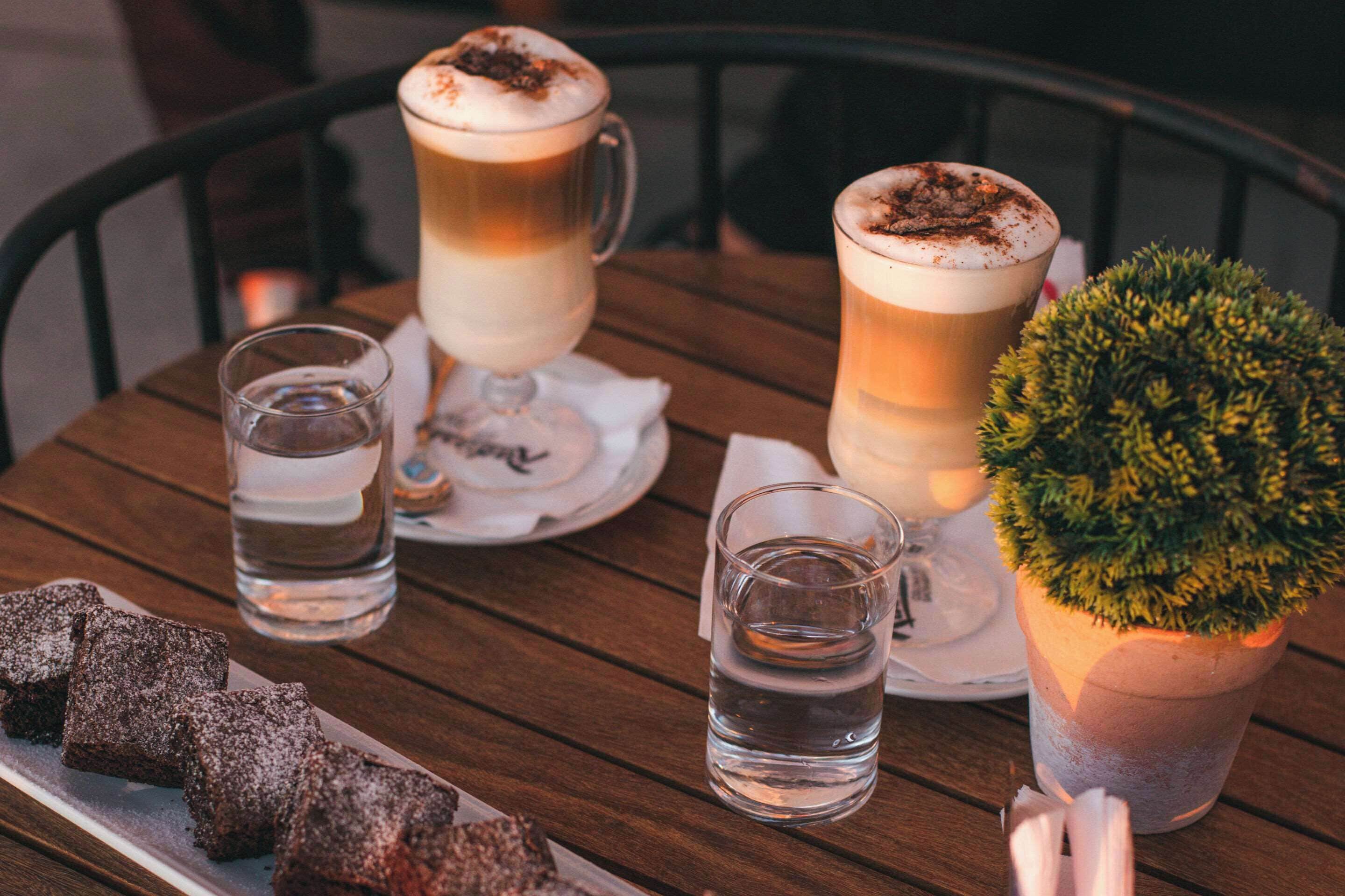 A wooden table with two glasses of beer, a small potted plant, and a plate of brownies.
