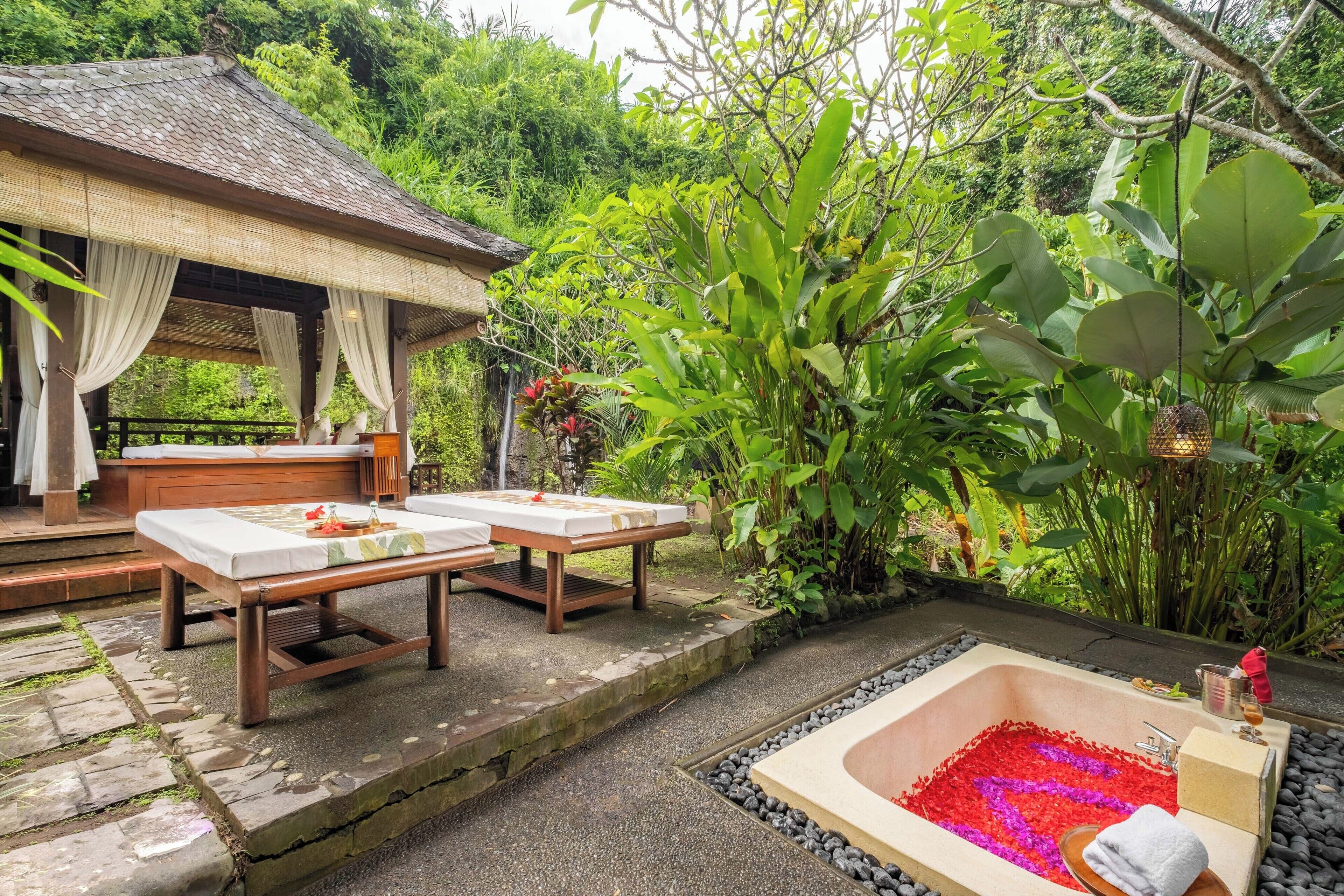 A spa area with a wooden bench, a massage table, and a bathtub filled with rose petals.