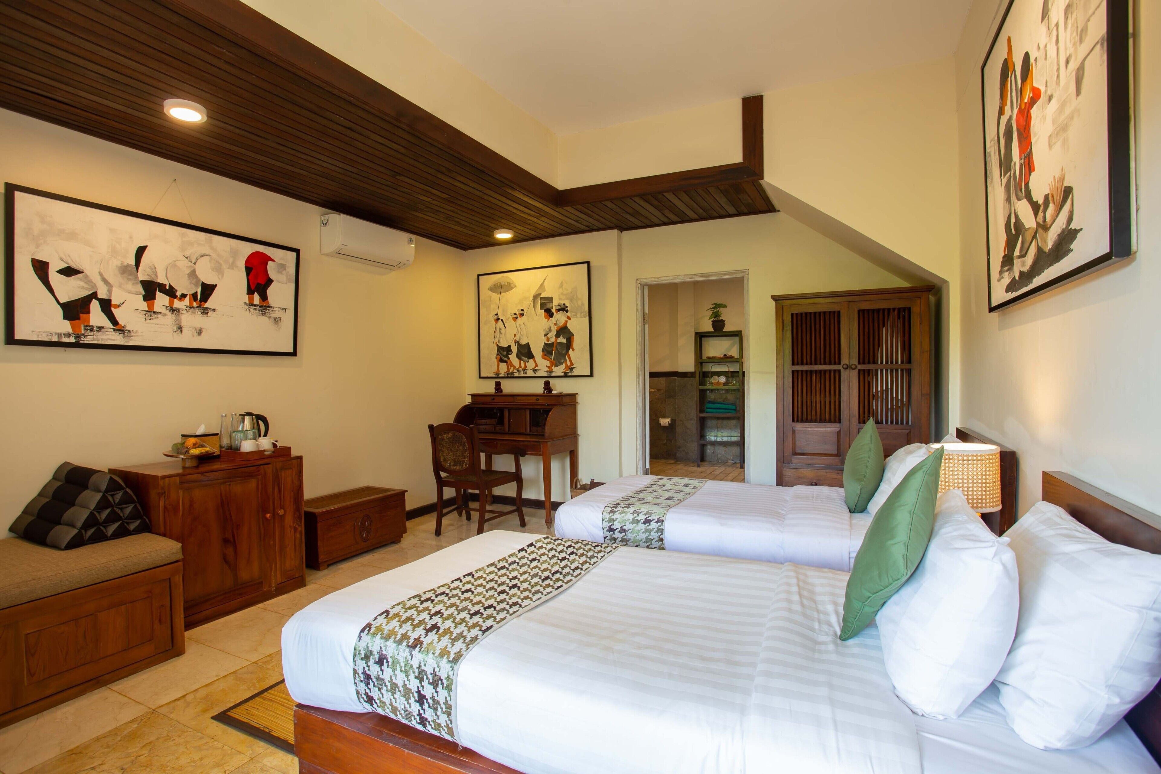 A hotel room with two beds, a desk, a chair, a sofa, and artwork on the walls.