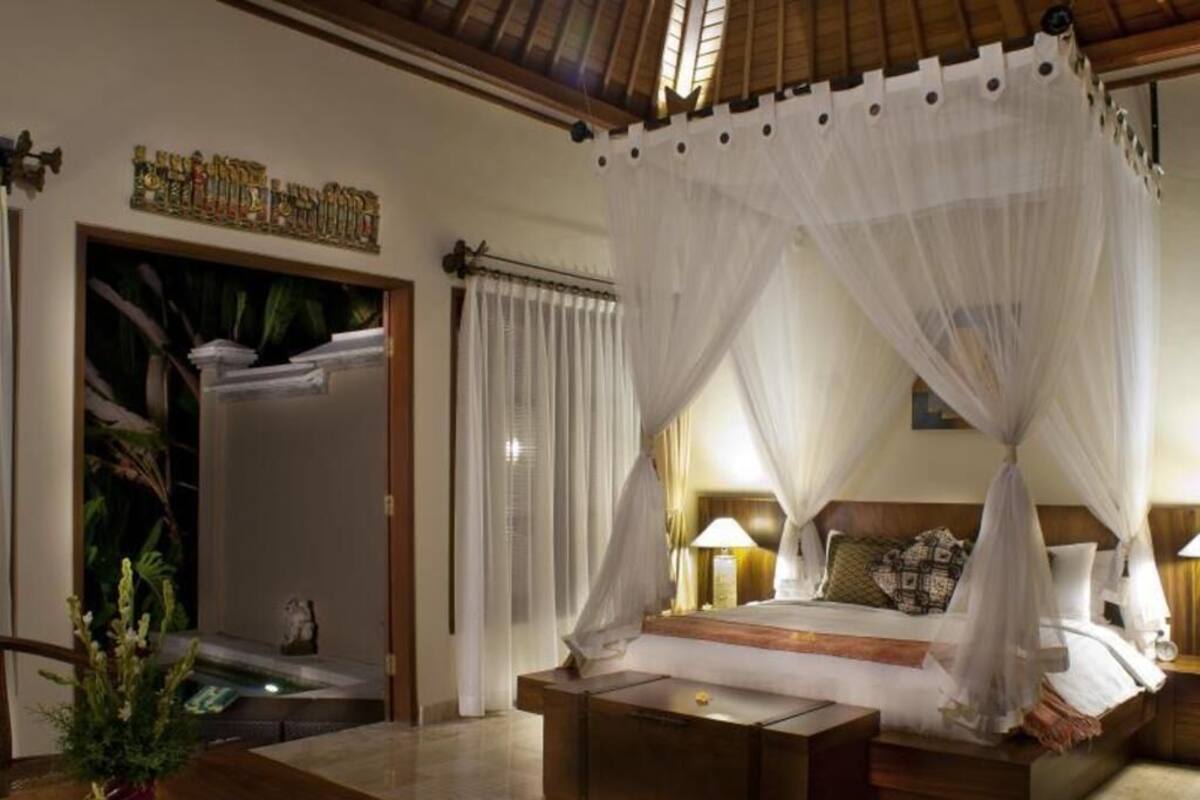 A room with a bed, a nightstand, a bedside table, a window with curtains, and a plant on a table.
