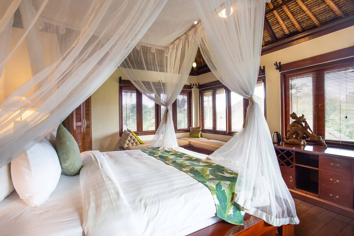 A bed with a canopy, a sofa, a wooden dresser, and a statue.
